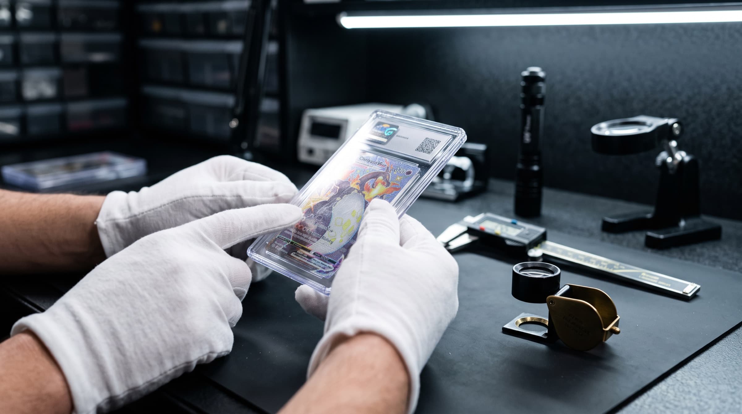 Gloved hands inspecting a slabbed card over a light pad with a loupe